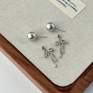Elegant grey pearl stud earrings with silver bow ribbon pendants on a neutral canvas