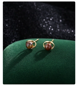 Détail macro de boucles d'oreilles planète en or avec pierre œil de tigre sur velours