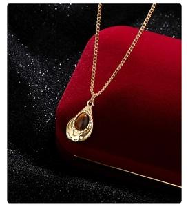 Detail of tiger eye stone teardrop pendant necklace resting on red velvet gift box