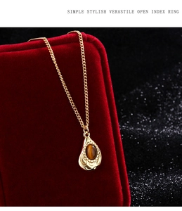 Detailed shot of golden teardrop necklace with brown tiger eye stone on red velvet