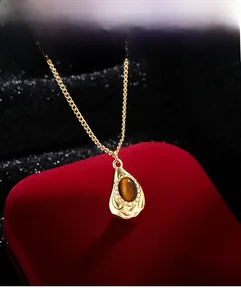 Macro shot of gold teardrop necklace featuring a brown tiger eye stone on red velvet box