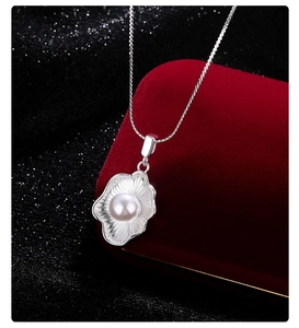 Detail of a shell-shaped silver pendant with a central pearl on a red velvet jewelry box