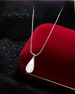 Primer plano de un colgante de gota de plata con piedra blanca sobre terciopelo rojo