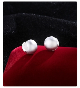 Macro view of minimalist silver frosted ball stud earrings on a red velvet surface