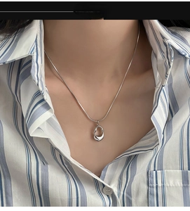 Close-up of minimalist silver irregular oval pendant on a sleek snake chain necklace
