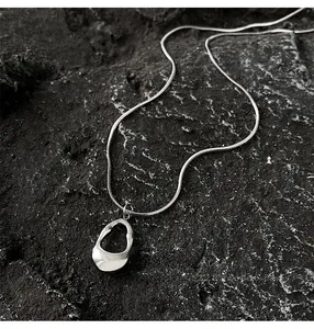 Macro shot of silver minimalist irregular hollow oval pendant on snake chain over black rock