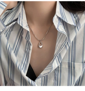 Close-up of a minimalist hollow oval pendant on a silver snake chain worn by a model