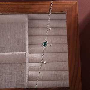 Elegant silver anklet with a green lotus charm and polished beads in a wooden box