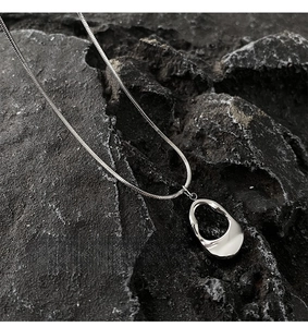 Macro shot of silver snake chain with polished irregular hollow oval pendant on rock
