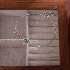 Elegant S925 silver anklet featuring a green lotus pendant and beads on beige fabric