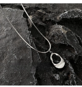 Macro shot of silver irregular hollow oval pendant on a sleek snake chain over grey stone