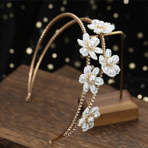 Elegant gold bridal headband with handmade pearl flowers and sparkling crystals on a stand