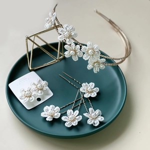 Detailed set of handmade white floral headbands and pearl earrings on ceramic plate