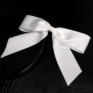 Elegant white satin bridal bow hair clip with long tails on a stylish black surface