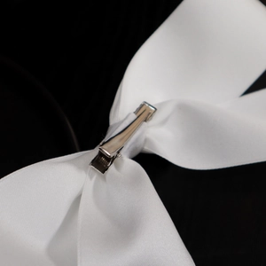 Detailed back view of a white satin bow hair clip with polished silver alligator clip