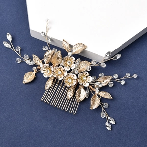 Detailed close-up of bridal hair comb with gold leaves, white enamel flowers and crystals