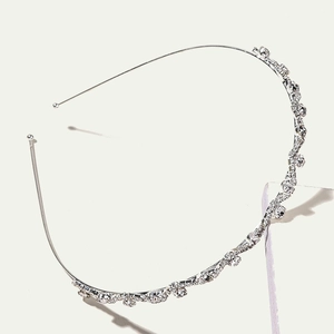 Elegant wavy silver alloy headband with sparkling rhinestones on a white pedestal