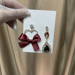 Detailed close-up of asymmetrical burgundy velvet bow earrings with heart and pear-shaped gems