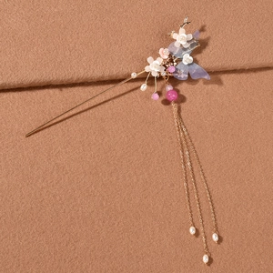 Detalle de pasador dorado con mariposa púrpura, flores blancas y borlas largas de perlas