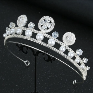 Close-up of luxury bridal crown with radiant zircons and white pearls on a black stand