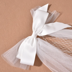 Elegant white satin bridal bow with layered mesh veil and mesh details on beige background