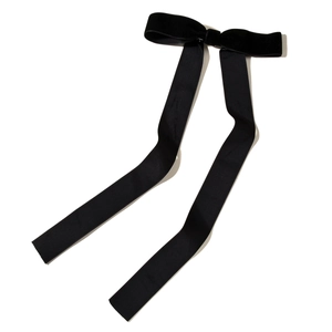 Detail of elegant black velvet bow hair clip with long flowing satin ribbons on white backdrop