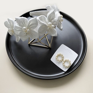 Elegant white camellia headband with pearl hoop earrings on a decorative black tray