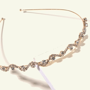 Gros plan d'un serre-tête doré ondulé avec strass brillants sur bloc géométrique blanc