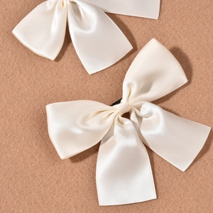 Set of two off-white satin bow hair clips for bridal wedding accessories on brown fabric