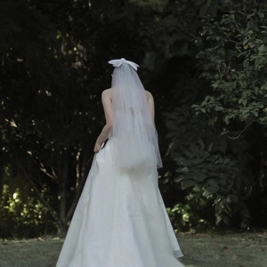 Elegant white satin wedding dress with a long tulle veil and a delicate bow hair accessory
