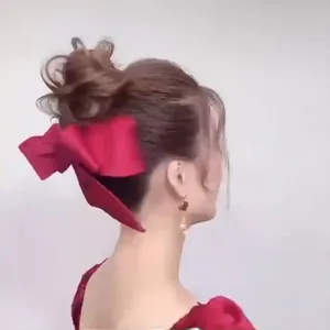 Close-up of a large red satin bow hair clip and heart pearl earrings on a model
