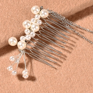 Close-up of elegant silver hair comb with white pearls and long tassel chains on camel fabric