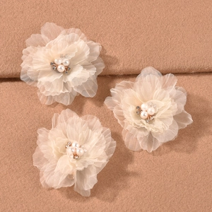 Detailed close-up of three cream ruffled flower hair clips with pearls on soft fabric