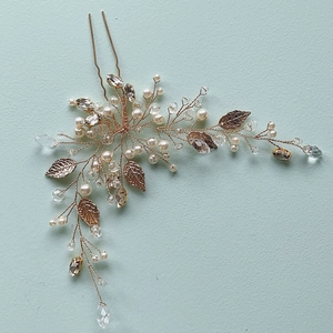 Macro detail of gold bridal hair pin with pearls, crystals, and delicate metal leaves
