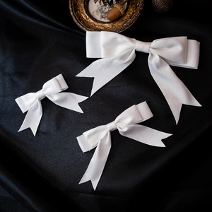 Three-piece set of elegant white satin bow bridal hair clips on black silk background