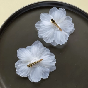 Detail of white organza flower hair clips with textured petals and gold metal alligator grip