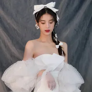 Detail of white bridal bow hair accessory and pearl earrings with puff sleeve dress