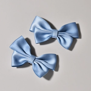 Detailed close-up of two light blue satin bow shoe clips with smooth silk texture