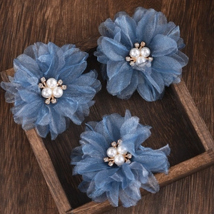 Detailed view of three blue textured fabric flower hair clips with pearls on wood