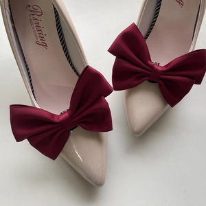 Macro shot of beige patent leather pointed heels with large burgundy ribbon bows