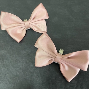 Detail view of pink satin bow shoe clips with silver metal duckbill buckles on a dark surface