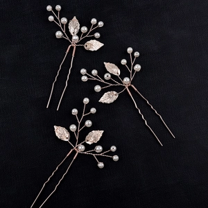 Detailed view of rose gold leaf hair pins with white pearls on black leather background