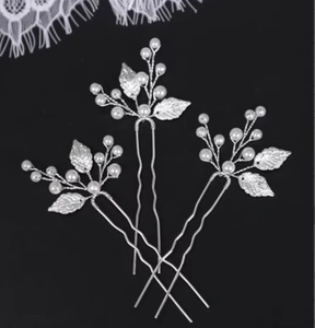 Detail of three silver leaf U-shaped hair pins with white pearls on black background