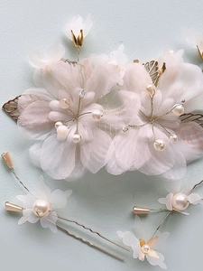 Set pettine sposa con fiori di organza bianchi, perle e foglie dorate su sfondo azzurro