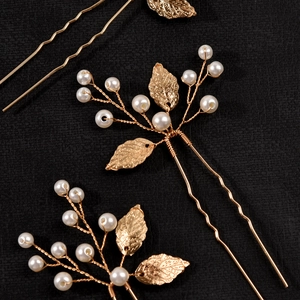 Detail of three golden leaf hair pins with white pearls on a dark textured background