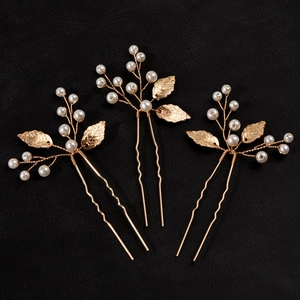 Detailed macro of golden metal leaf hair pins with white pearls on a black background