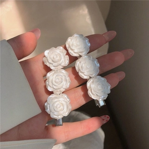 Detail showing two pearlescent white rose hair clips with silver metal duckbill base