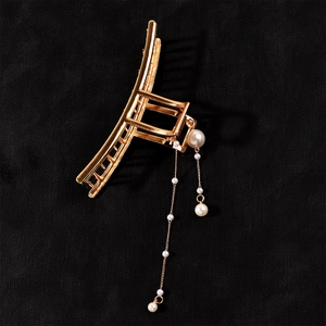 Detail of golden alloy hair claw clip featuring elegant hanging faux pearl tassels