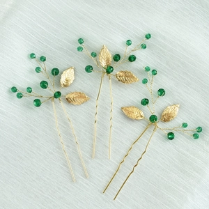 Detailed macro of golden leaf hairpins with emerald crystals and handmade pearl accents