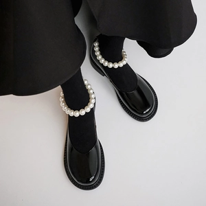 Close-up of black patent leather Mary Jane shoes with elegant white pearl ankle straps